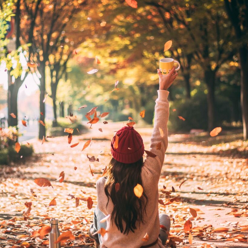 落ち葉の中で喜ぶ女性の後ろ姿